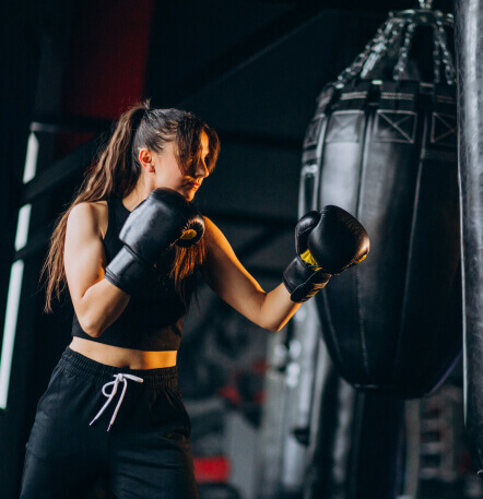 Mujer joven entrenando boxeo en un gimnasio, usando guantes de boxeo y golpeando un saco de boxeo.