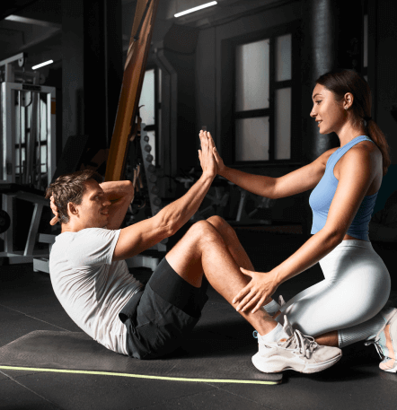 Entrenador personal asistiendo a un hombre en una rutina de abdominales en un gimnasio moderno, enfocándose en la técnica y la motivación.